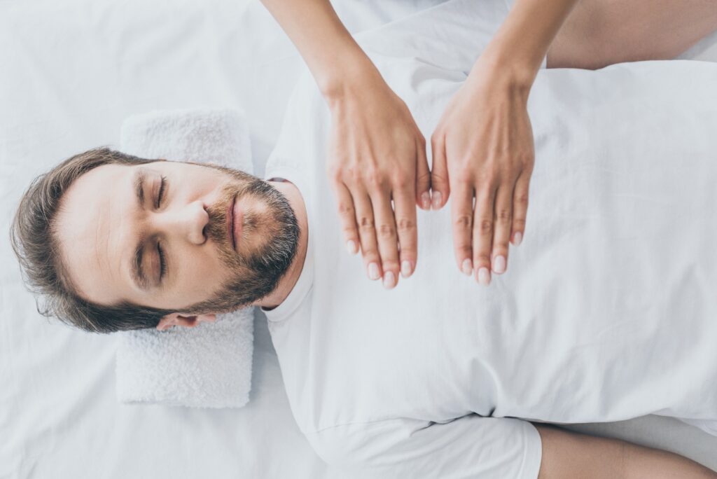 top view of bearded man with closed eyes receiving reiki treatment